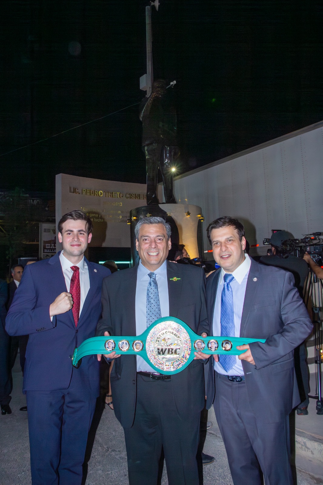 Tres asistentes frente al monumento de Pedro Treto Cisneros con un cinturón de campeonato