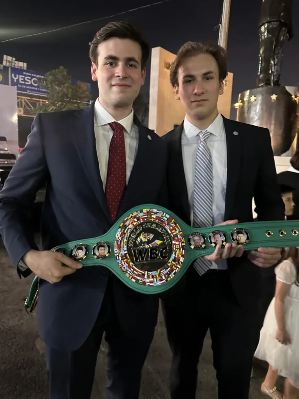Dos asistentes sostienen un cinturón WBC frente al monumento