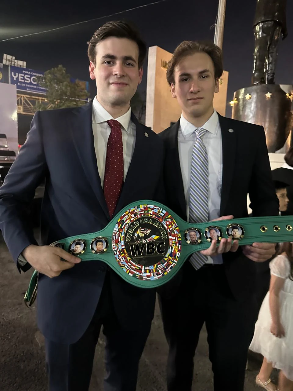 Dos asistentes sostienen un cinturón WBC frente al monumento