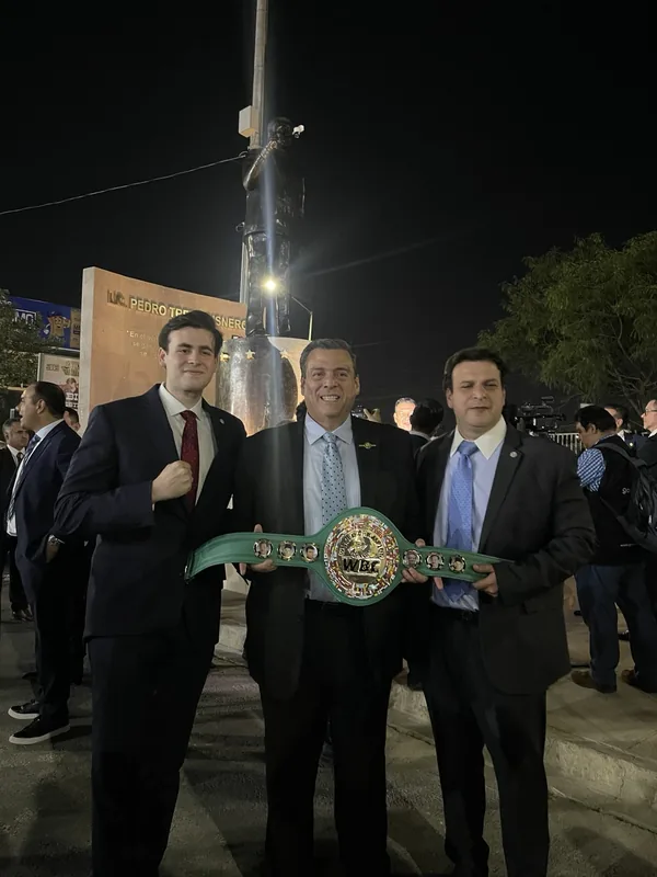 Tres asistentes sostienen un cinturón WBC frente al monumento